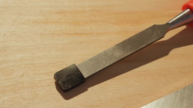 Close up shots focus on metal woodworking chisel with black handle tip resting steadily on light wood. scene emphasizes sharp edge smooth texture of both wooden and metallic surfaces