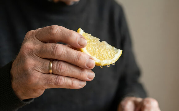 Elderly man squeezing a fresh lemon slice with juice dripping, representing healthy eating and cooking concepts