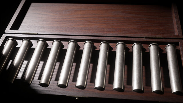 Rank of plain pewter pipes standing in a dark timber case under hard raking light with copy space
