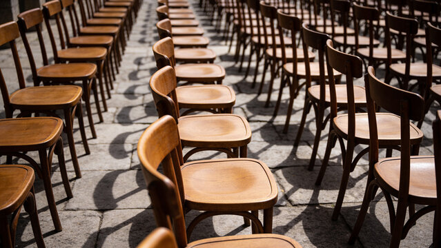 Rows of plain empty wooden chairs receding down a bare stone aisle in hard low side light