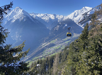 Gondola transportation solution: Yellow cable car gondola suspended over alpine valley with snow-capped peaks and village in Mayrhofen, Tyrol, Austria © Alexander Will