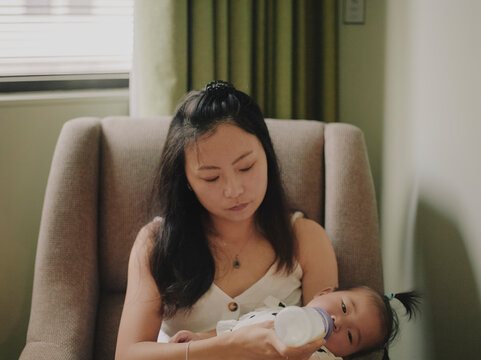 Mother bottle-feeding her newborn baby while sitting in a comfortable armchair at home