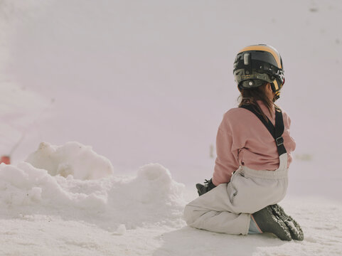 Young child in a ski helmet sitting in the snow seen from behind at Chamrousse