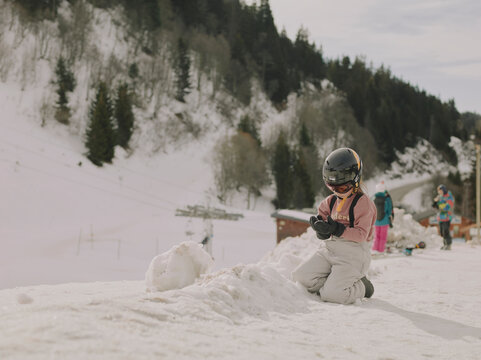Child in ski helmet kneeling in the snow making a snowball at Chamrousse