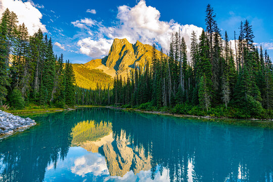 Sunlit mountain peak mirrors in turquoise Emerald Lake, framed by evergreen forest in Yoho National Park, BC.
