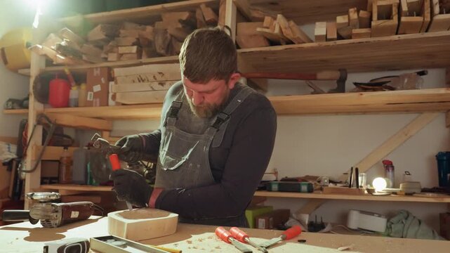 Carpenter works on detailed joinery in his workshop. Man uses hand tools like chisels and mallets to shape wood surrounded by variety of traditional craftsmanship materials and equipment