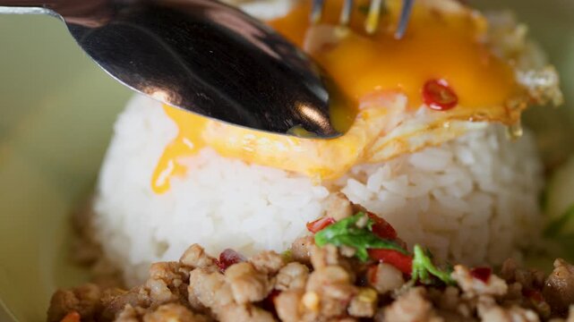 Spoon Piercing Fried Egg Yolk on Thai Pad Krapow Rice