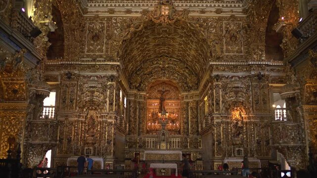 The gold carved baroque interior and main altar of the Church of Sao Francisco in Salvador, with small visitors below, Brazil