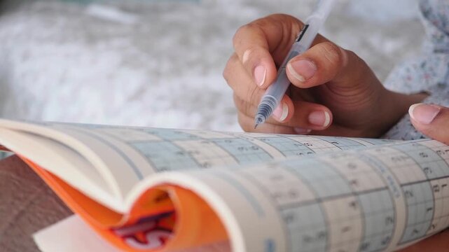 Person Solving a Sudoku Puzzle in a Book