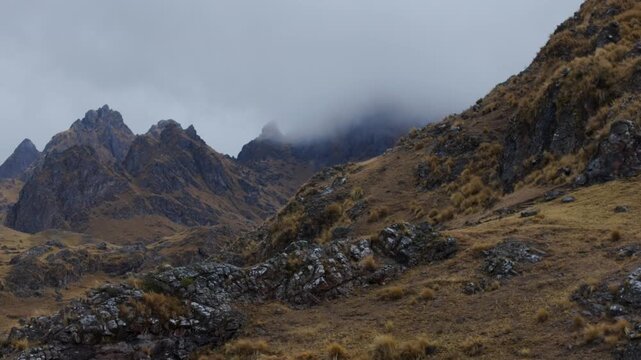 Cinematic view of jagged Andean mountain crags and rocky high-altitude slopes shrouded in low misty clouds in the rugged wilderness of Cusco region, Peru