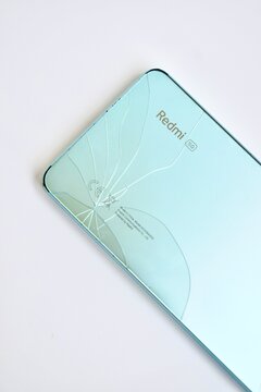 Kelantan, Malaysia - 24 August 2026: Close-up of a light blue smartphone back glass panel featuring a distinct crack pattern near the camera module over a clean white background.