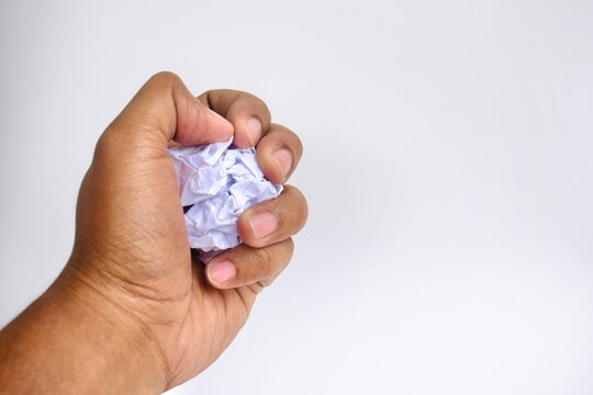 Close-up of a human hand squeezing a crumpled piece of paper against a plain white background, symbolizing frustration, stress, or rejected ideas.
