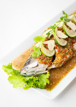 Thai steamed whole sea bass, spicy lime sauce, garlic, chili, and coriander topping on a traditional ceramic plate, authentic exotic seafood dish, steamed seabass with lemon sauce