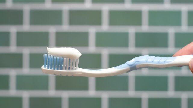 Toothbrush with white toothpaste close-up against a background of green tiles.