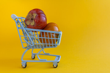 Miniature shopping cart holding two ripe persimmons on yellow background © Irina