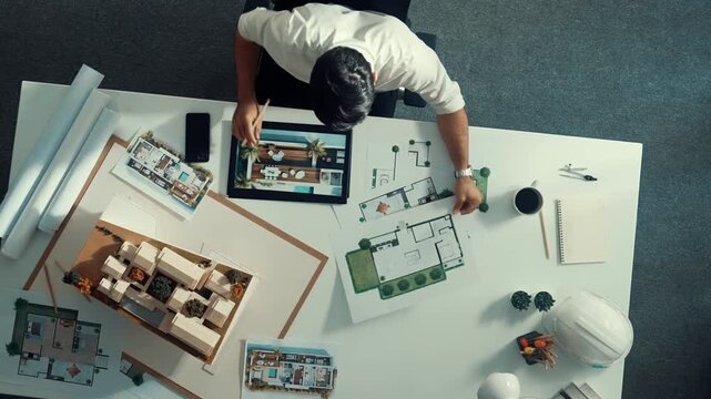 Top view of business man using tablet plan house design while sitting at meeting table with blueprint and equipment scatter around. Aerial view of civil engineer working at blueprint. Alimentation.