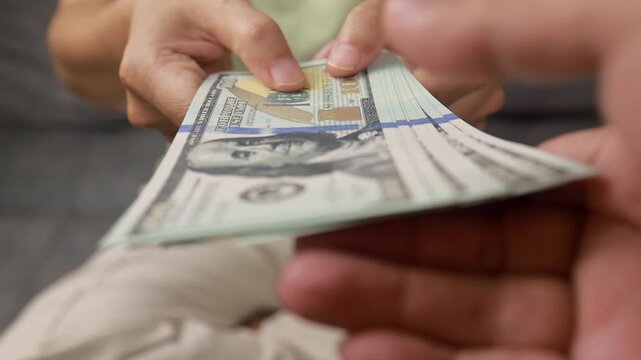 Person handing over a stack of hundred dollar bills to someone