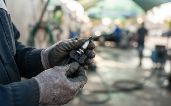 Mechanic holding a TPMS tire pressure sensor in an auto repair shop representing automotive maintenance and service