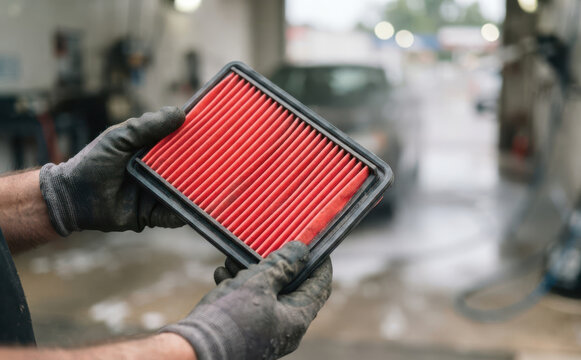 Mechanic holding a new red car air filter in an auto repair shop showing automotive maintenance