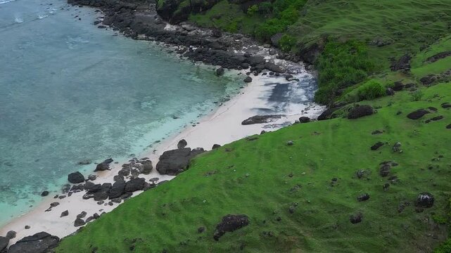 Aerial seascape cove with turquoise water, drone view of pristine sand pocketed between rocky headlands and lush green slopes, gentle waves lapping shoreline, cinematic tranquil mood, Lombok