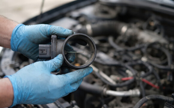 Mechanic holding a mass air flow sensor in hands over car engine bay for automotive repair and maintenance