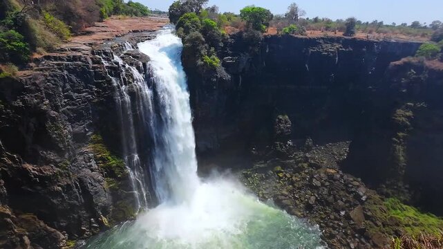 Slow motion pan across Victoria Falls, Zimbabwe, revealing cascading water, exposed cliffs and a misty gorge during the dry season.