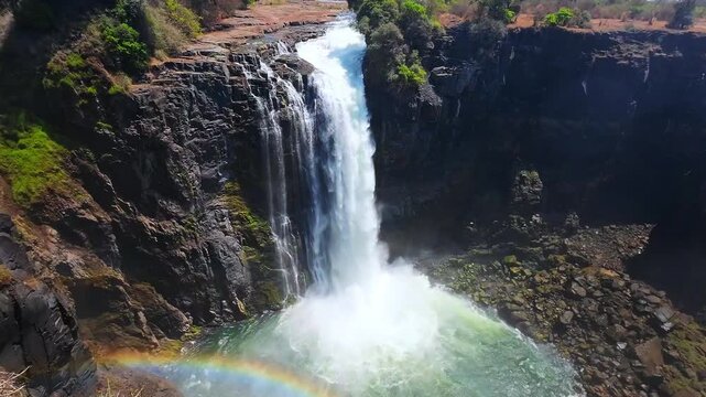 Water plunges into a rocky pool in slow motion at Victoria Falls, Zimbabwe, with a rainbow in the spray during the dry season.