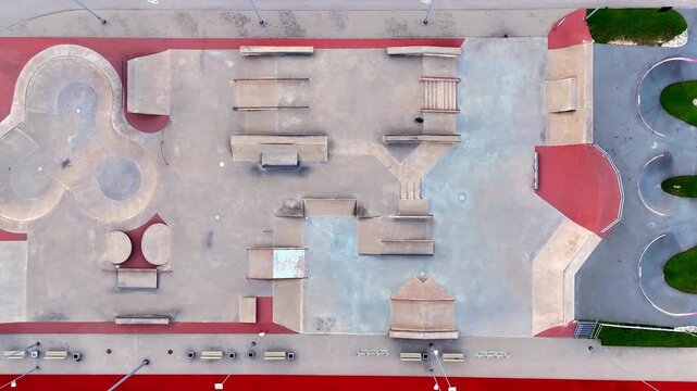 Straight-down drone view of a large empty skatepark featuring bowls, rails, stairs, ramps and geometric concrete obstacles within a modern urban recreation complex.