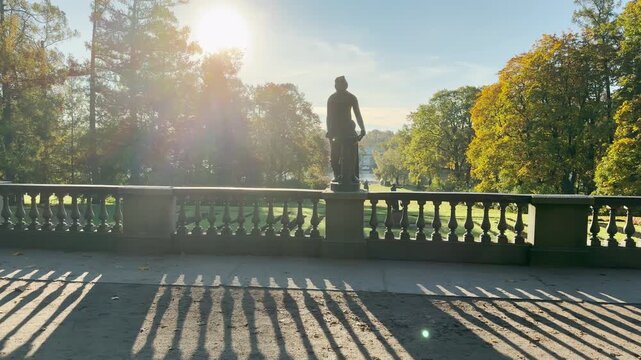 Tracking shot of an empty sunlit terrace on gimbal. Smooth sideways camera movement reveals statues and golden autumn in Catherine Park, Pushkin, Saint Petersburg, evoking deep peace.