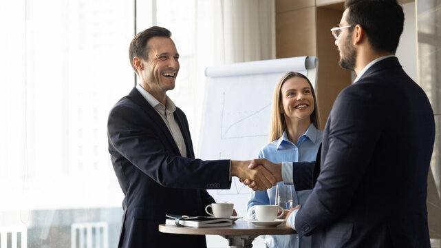Group of happy multiethnic businesspeople shaking hands during professional meeting in corporate office. Handshake as agreement, closing deal and successful partnership sign. Business, collaboration