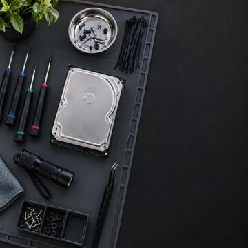 Precision screwdrivers, hard drive, screws, cable ties flashlight on black antistatic mat, top view, copy space