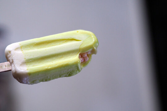 close-up shot of a green and white ice cream bar showing a bite mark with small pink candy fillings inside