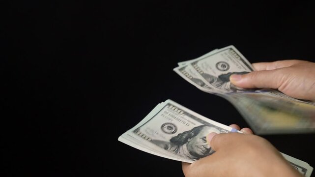 Hands counting hundred dollar bills on black background