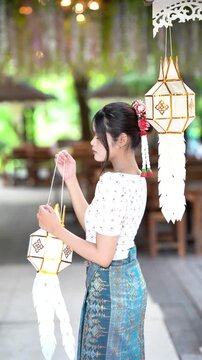 Slow motion of a beautiful Asian woman in traditional Lanna dress holding a Lanna paper lantern at Wat Ton Kwen, Chiang Mai, Thailand.