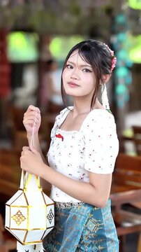 Slow motion of a beautiful Asian woman in traditional Lanna dress holding a Lanna paper lantern at Wat Ton Kwen, Chiang Mai, Thailand.