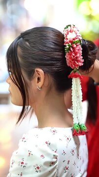 Slow motion of a young Asian woman adjusting a traditional Thai flower garland in her hair for a photoshoot.