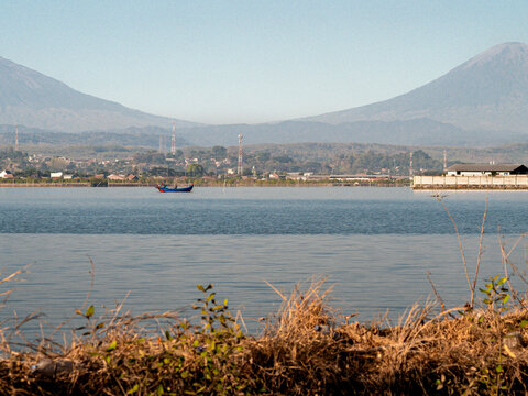 Scenic view of Kendal coast with twin volcanoes Mount Sindoro and Mount Sumbing gap, industrial area, and fishing boat, Central Java, Indonesia.