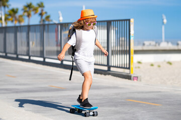 Child on a skateboard in motion. Blonde child with skateboard in sunlight. Child riding a skateboard in casual clothing. Stylish child on skateboard outdoors. Kid skateboarding. Casual kids clothing. © Volodymyr