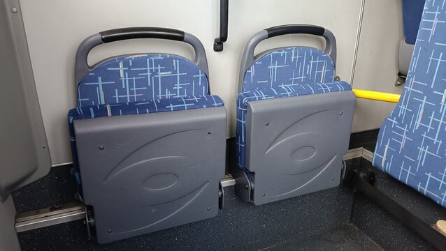 Empty blue folding seats inside public transport bus or train interior, commuting urban transit passenger horizontal view.