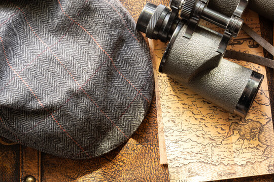 Old vintage maps, flat cap and binoculars on top of a vintage leather luggage case. Vintage travel background backdrop concept.