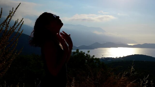 Silhouette of a woman suffering from the heat. Silhouetted woman fans her face with her hands to create a breeze and cool down, set against a seascape