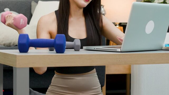 Asian Woman Exercising with Dumbbell While Working on Laptop at Home