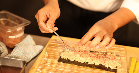 Chef Preparing Spicy Tuna Sushi Roll on Bamboo Mat in Restaurant © blueringmedia