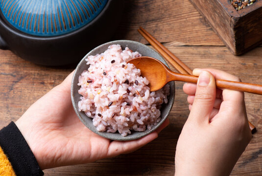 Hands serving cooked multigrain rice from a bowl