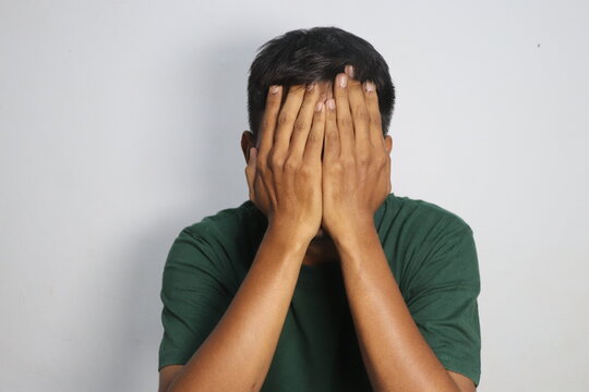 Stressed young man hiding his face with both hands in despair