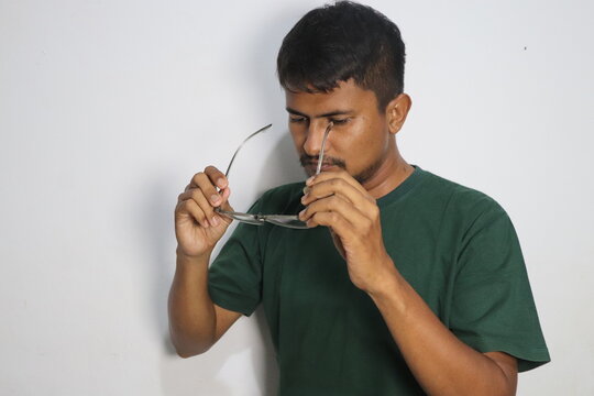 Young man holding eyeglasses while looking down against a white wall