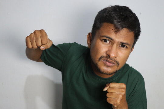 Young man punching forward with aggressive expression wearing green shirt indoors