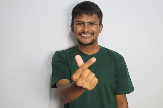 Young man smiling and making mini heart hand sign against white wall