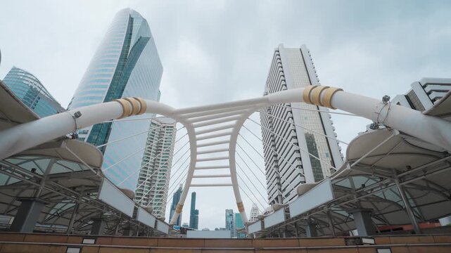 Modern bridge arches frame towering city buildings. Cloudy sky adds soft, diffused urban atmosphere