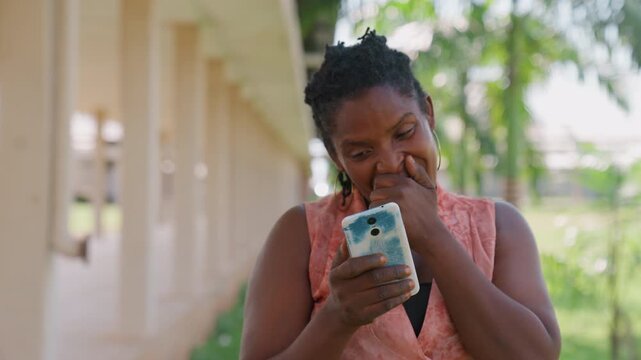 Lady stands outside under open structure with greenery in background. Woman holds phone case that is blue and white appearing to be engaged or amused by its content
